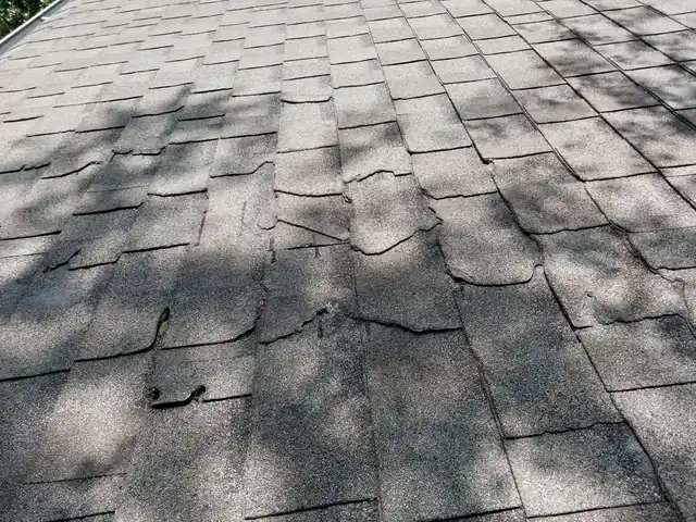 Close-up of worn asphalt shingles with cracked and missing pieces